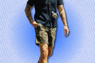 man wearing a navy sweater polo, camo shorts, and a camera across his chest