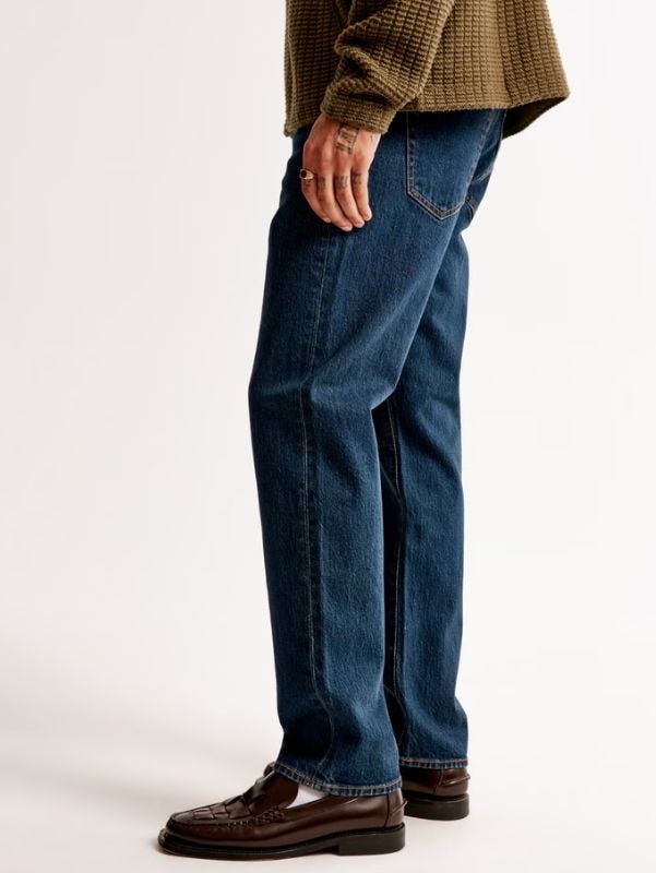 man from the waist down wearing dark blue jeans, a brown sweater and brown leather loafers