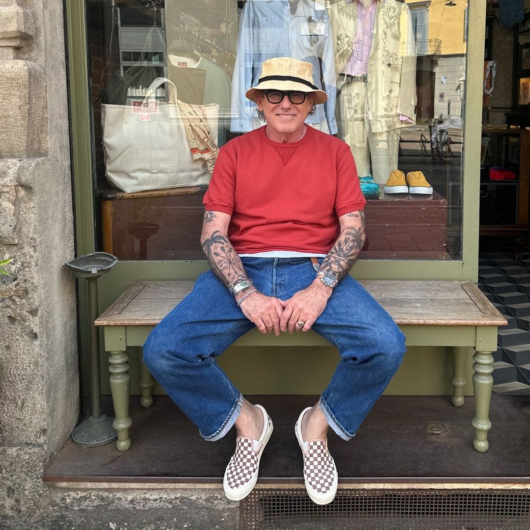 stylish older man wearing brown and white checkered vans sneakers with blue jeans and a red short-sleeve sweatshirt