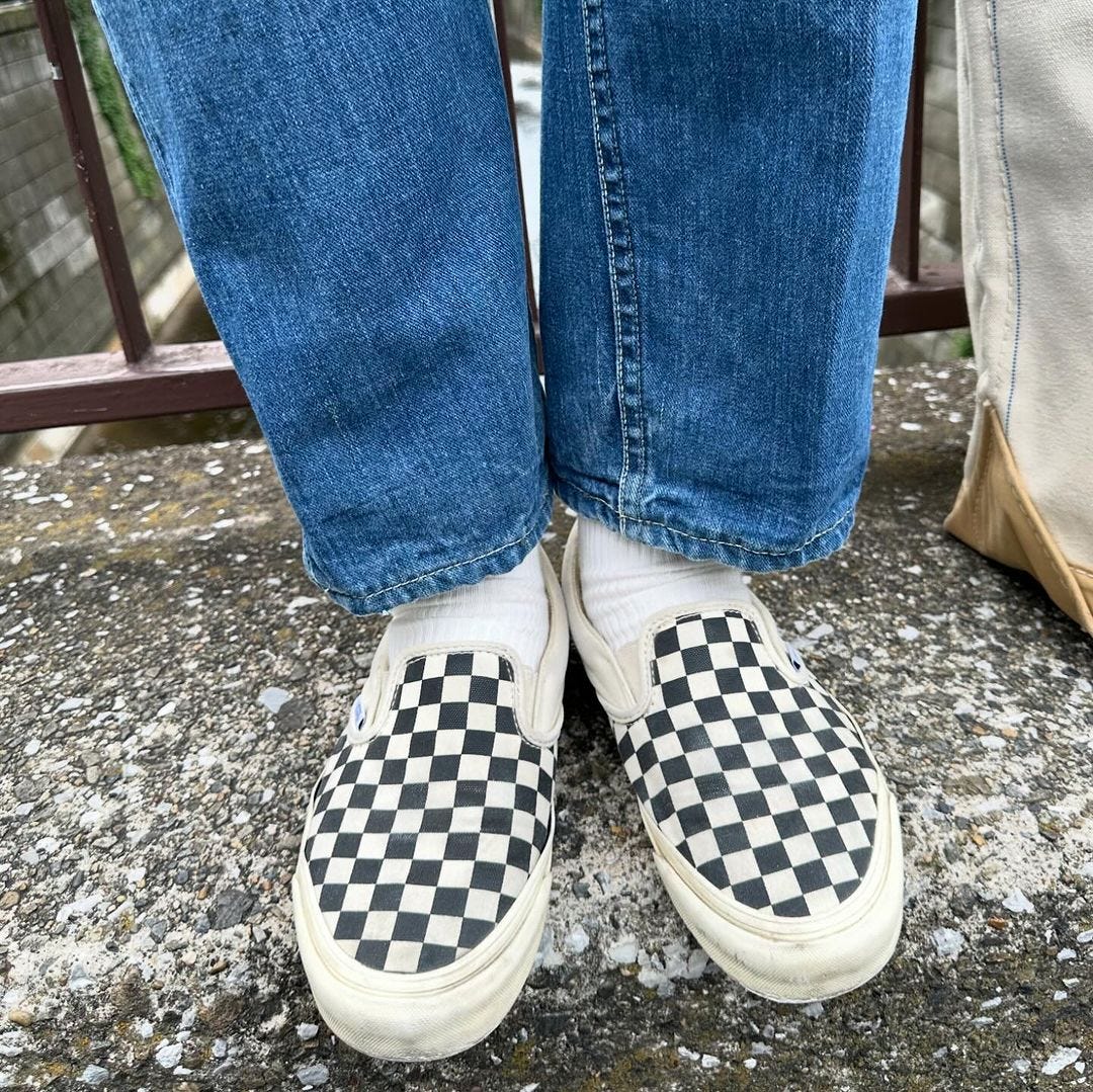 close-up of a man wearing jeans, white socks, and black and white checkered vans slip-on sneakers