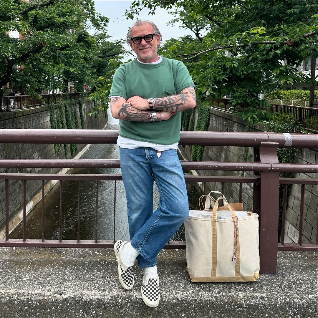 stylish older man wearing a green short-sleeve sweatshirt over a white t-shirt with blue jeans and checkerboard vans slip-on sneakers with white socks