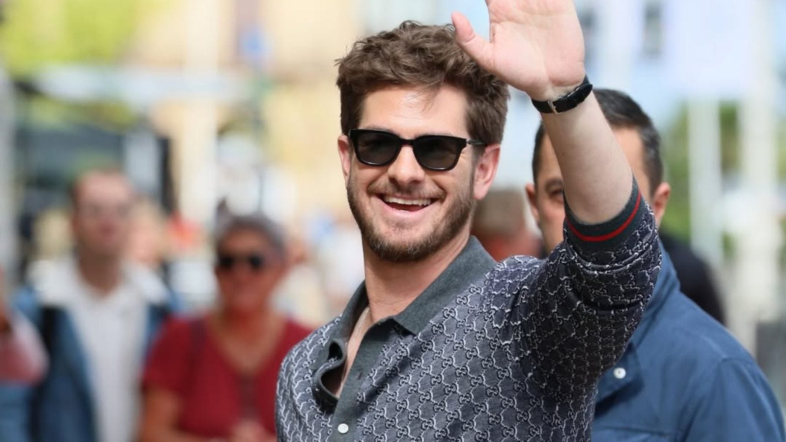 close-up of the actor andrew garfield, smiling and waving while wearing sunglasses