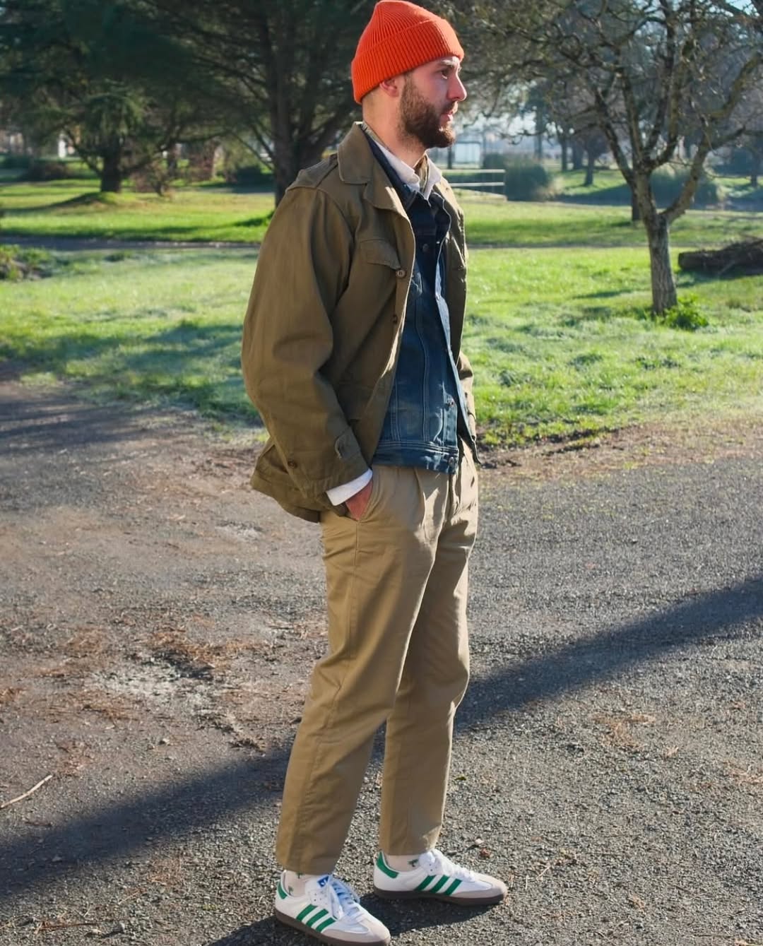 stylish man wearing white Adidas Samba sneakers with green stripes, tan chinos, a denim jacket, and orange beanie