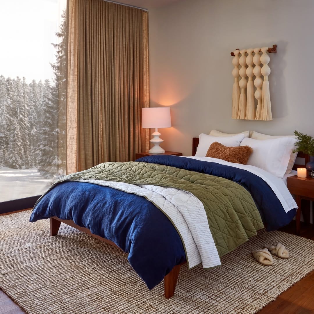 a bed made up with a blue comforter, topped with white and green quilts