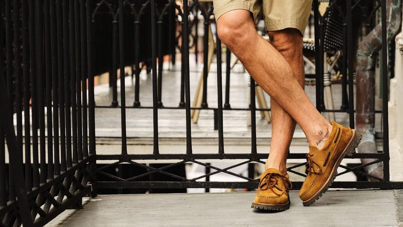 close-up image of a man from the knees down, wearing suede boat shoes and standing on a terrace outside