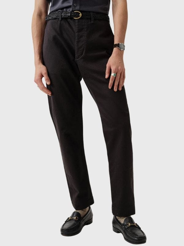 man from the waist down wearing a pair of black chinos with a black leather braided belt and black loafers