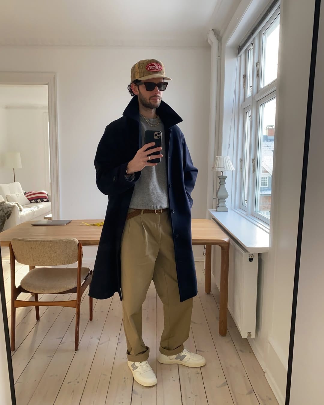 stylish man wearing a navy topcoat, grey crewneck sweater, tan pleated chinos, and new balance ct500 sneakers 