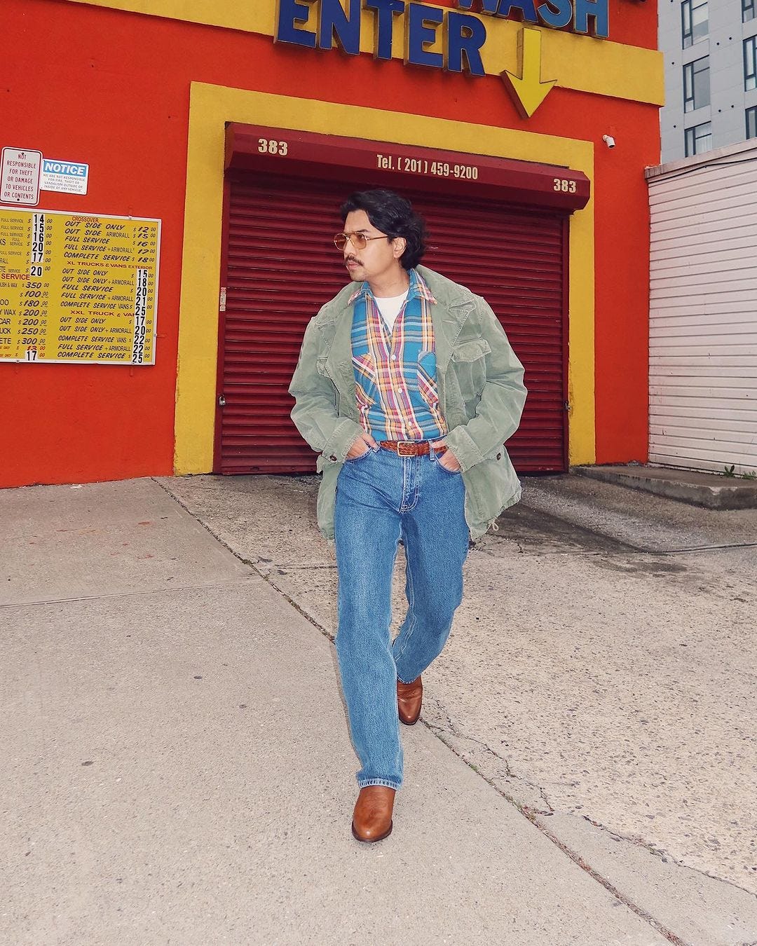 man wearing jeans, cowboy boots, a plaid shirt, and military-style green jacket