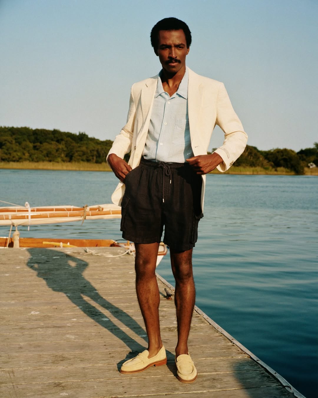 stylish man wearing a cream-colored blazer with black hybrid drawstring shorts and light suede loafers