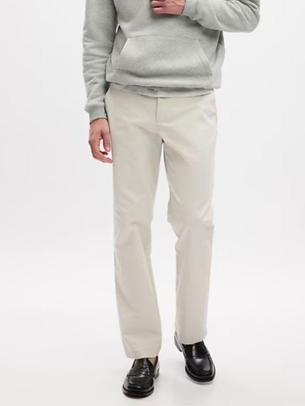 man from the chest down wearing a grey hoodie and light chinos with black loafers