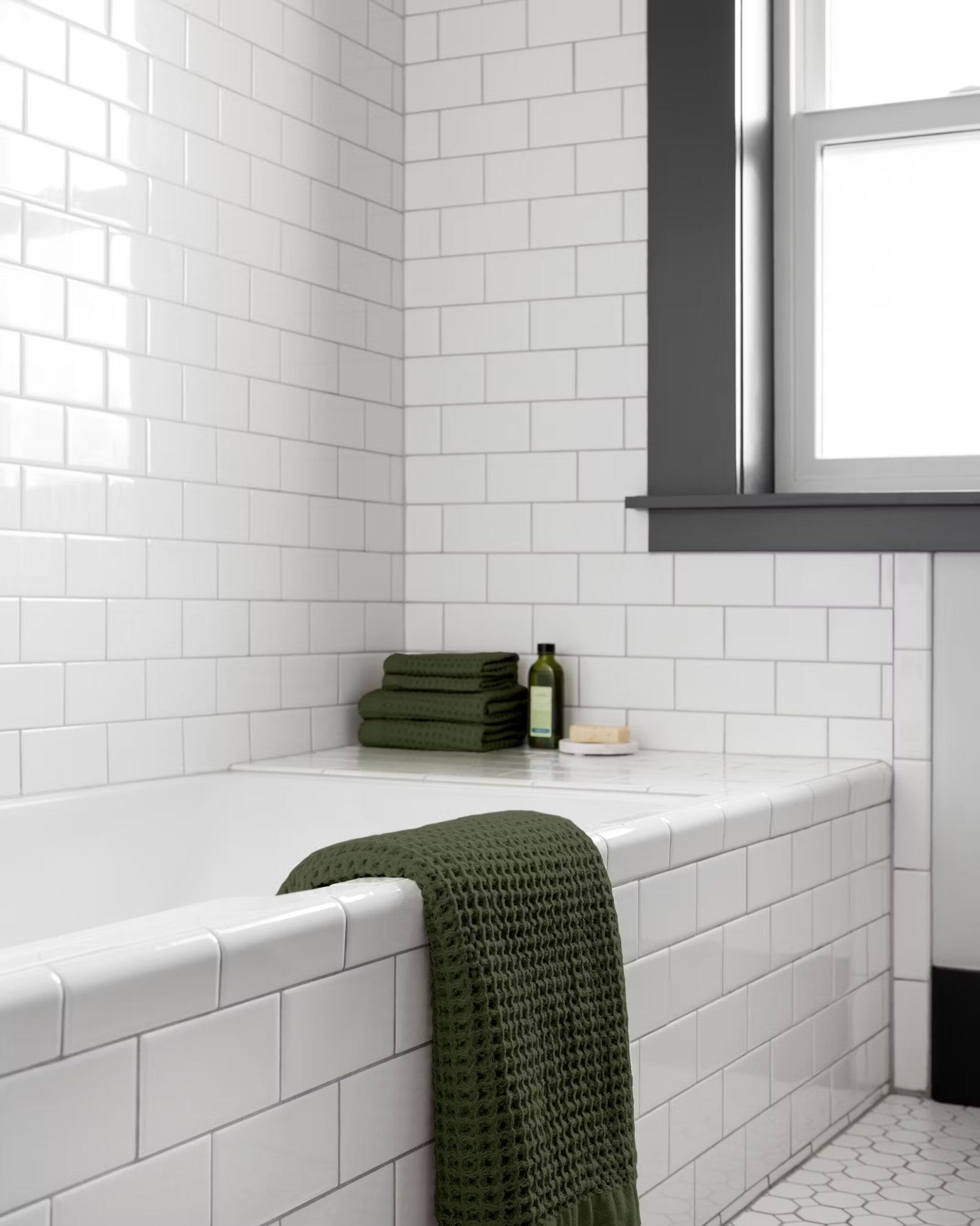 waffle-weave green bath towel draped over a white tiled bathtub