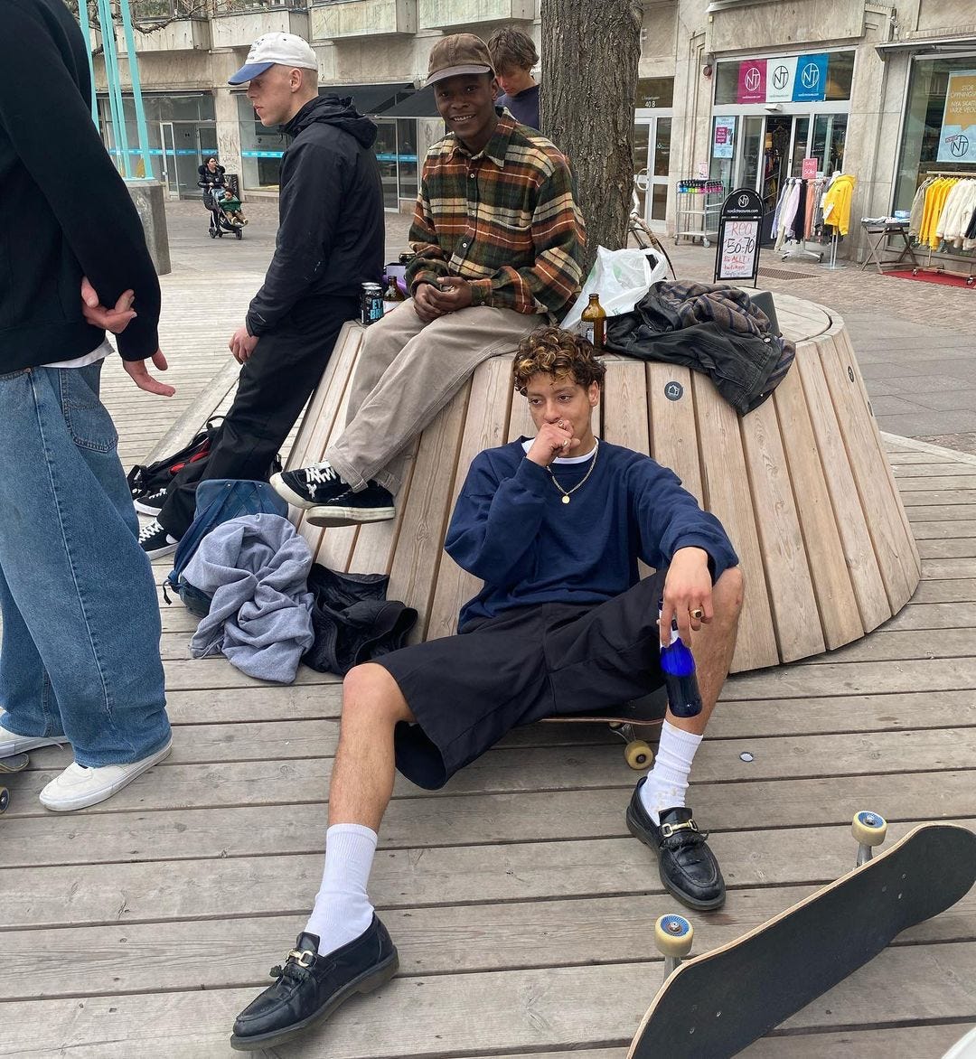 young man lying down wearing a dark shirt and baggy shorts with white socks and black loafers