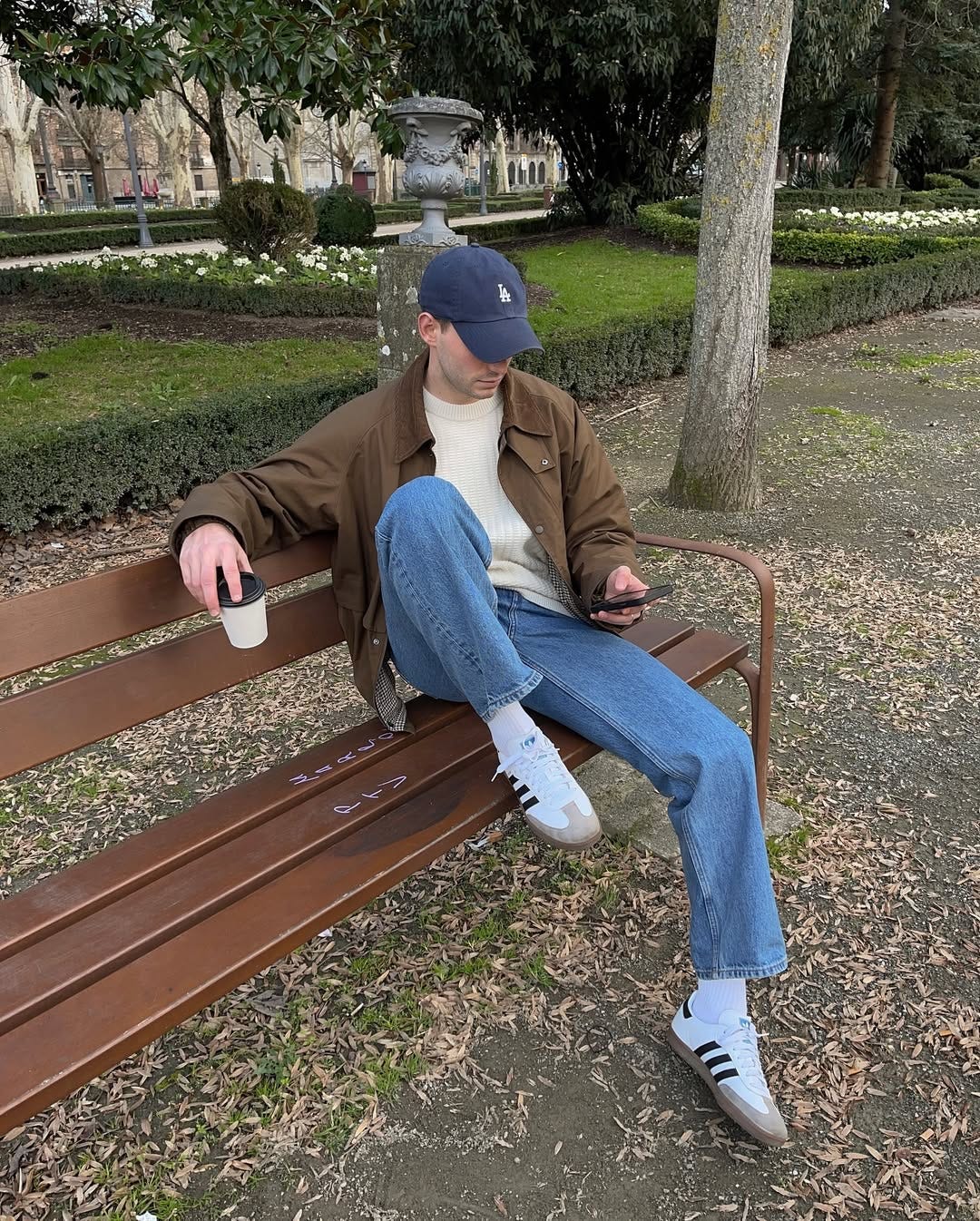 stylish man wearing white Adidas Samba sneakers with blue jeans, a cream sweater and brown waxed jacket