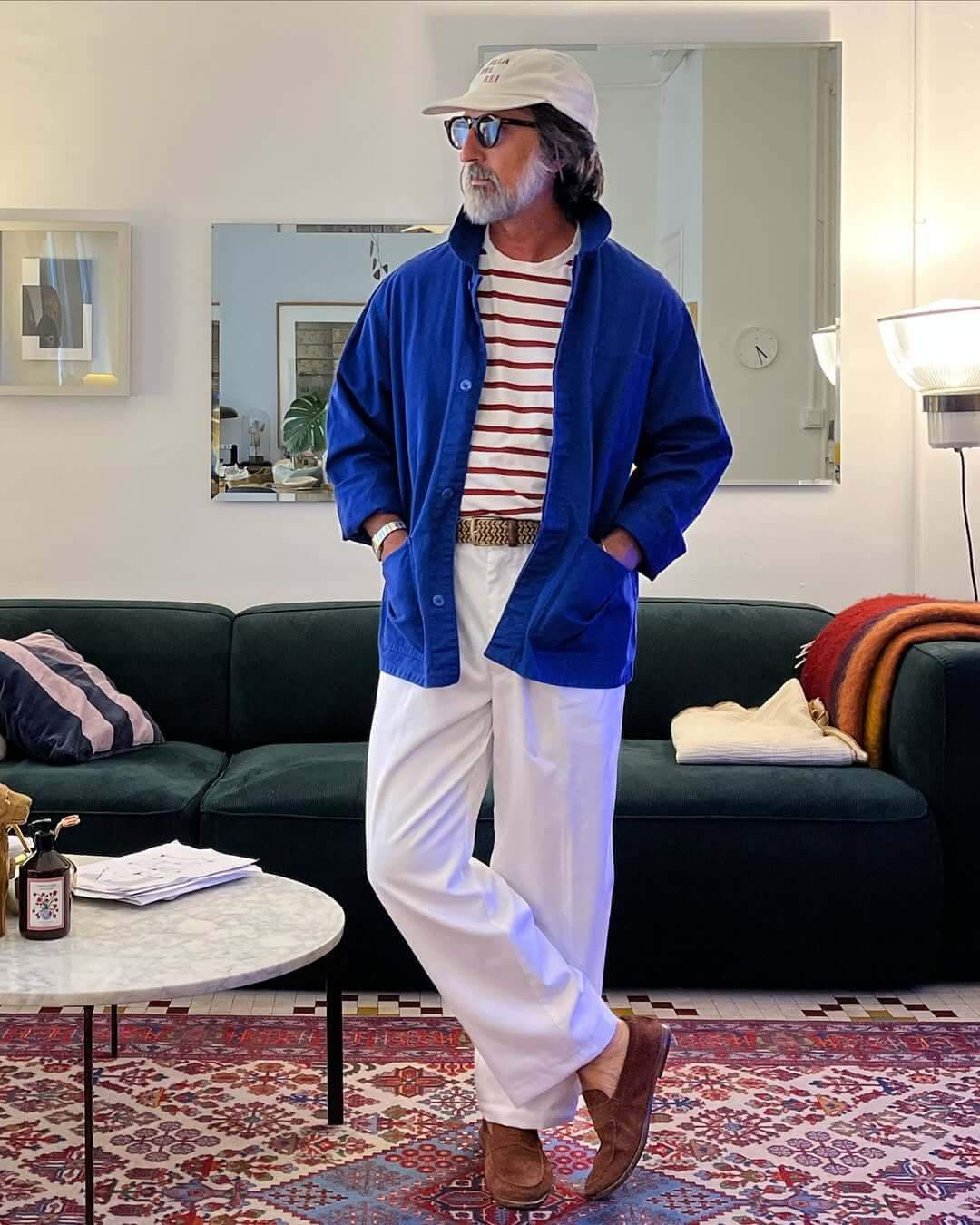 stylish man wearing a blue chore coat over a red and white striped tee with wide-leg white pants and brown loafers