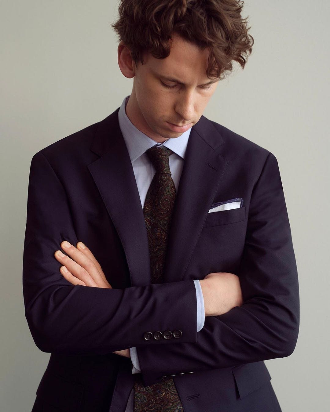 close-up of a stylish man wearing a navy suit jacket with a light blue dress shirt and paisley tie