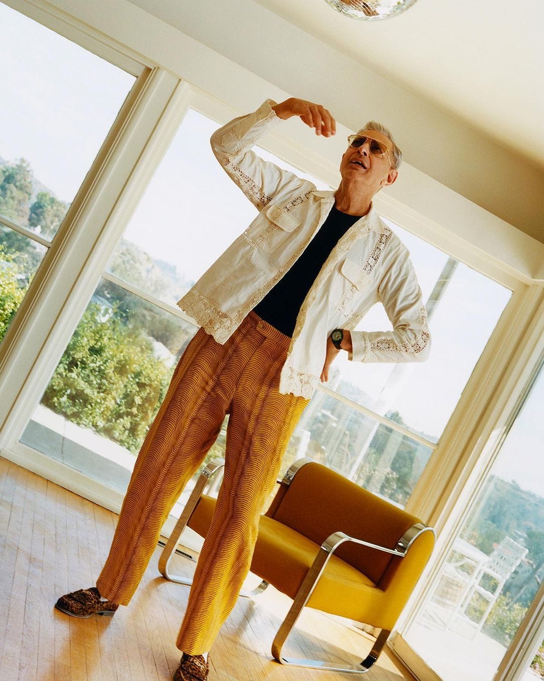 the actor Jeff Goldblum in a patterned overshirt, black shirt, and brown textured pants with tassel loafers