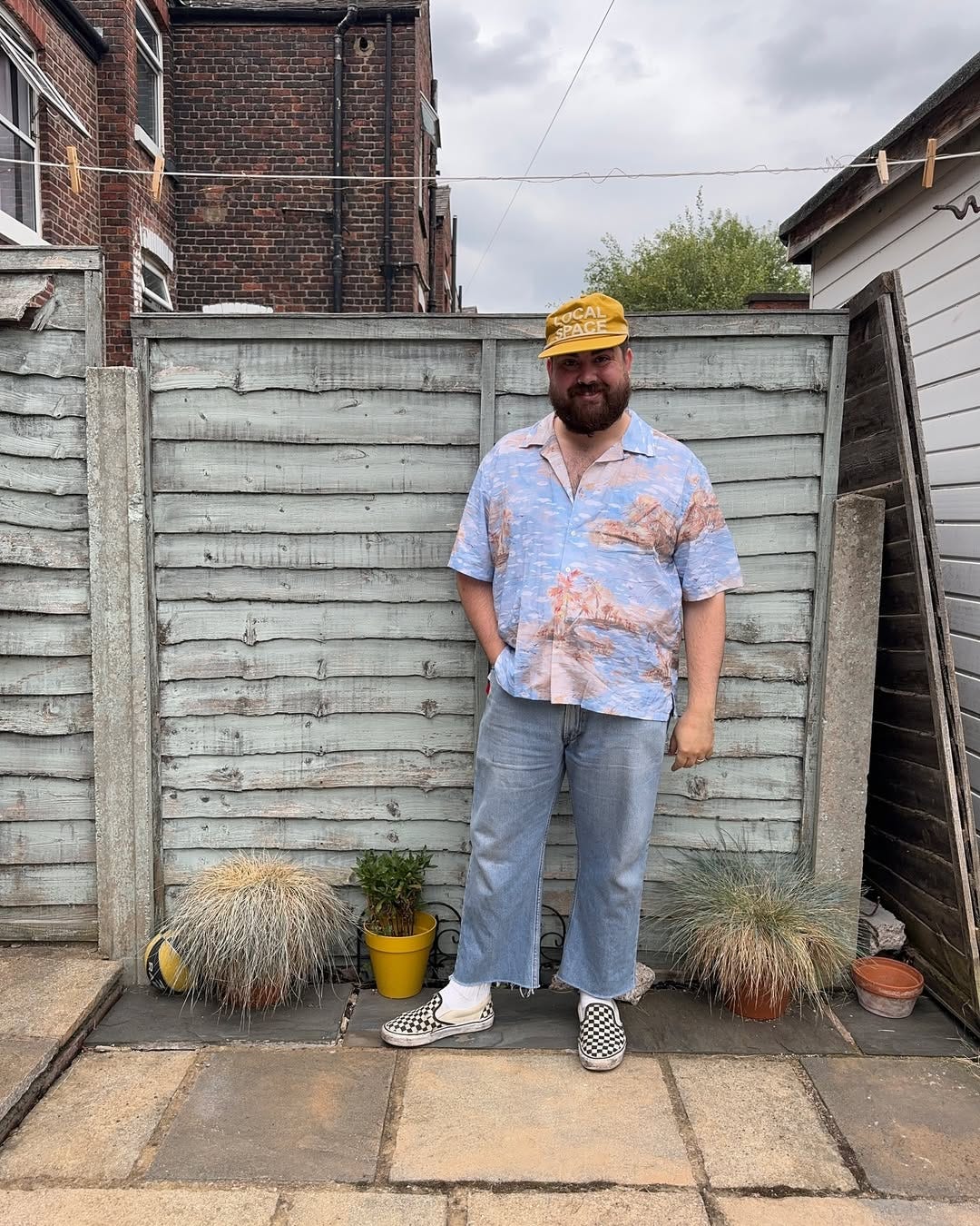 stylish man wearing black and white checkerboard vans sneakers with frayed hem jeans and a patterned camp shirt
