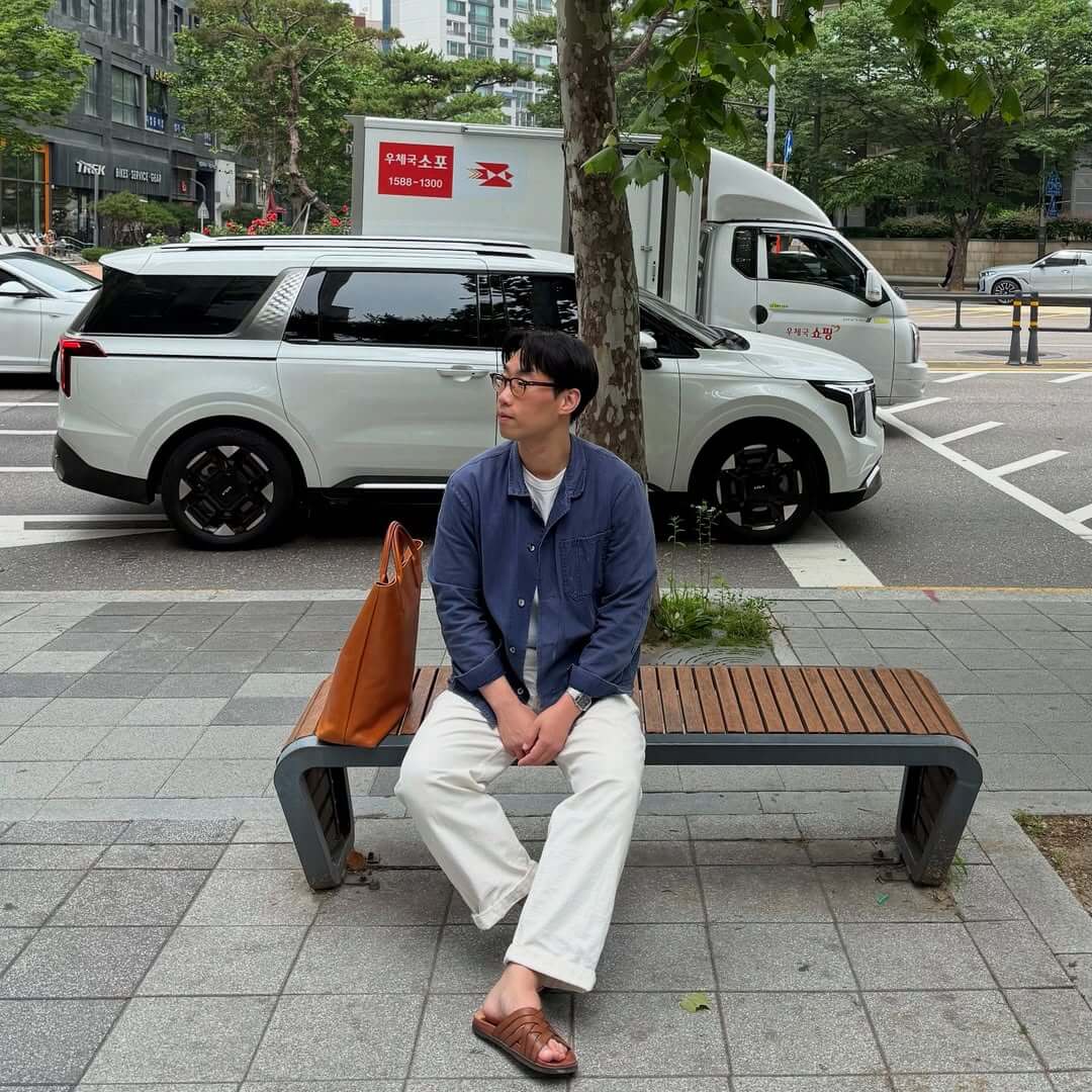 stylish man wearing a blue chore coat, white jeans, and brown leather sandals