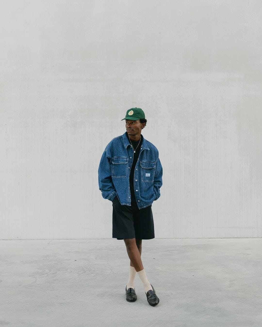 man in a denim jacket and dark shorts with white socks and black loafers