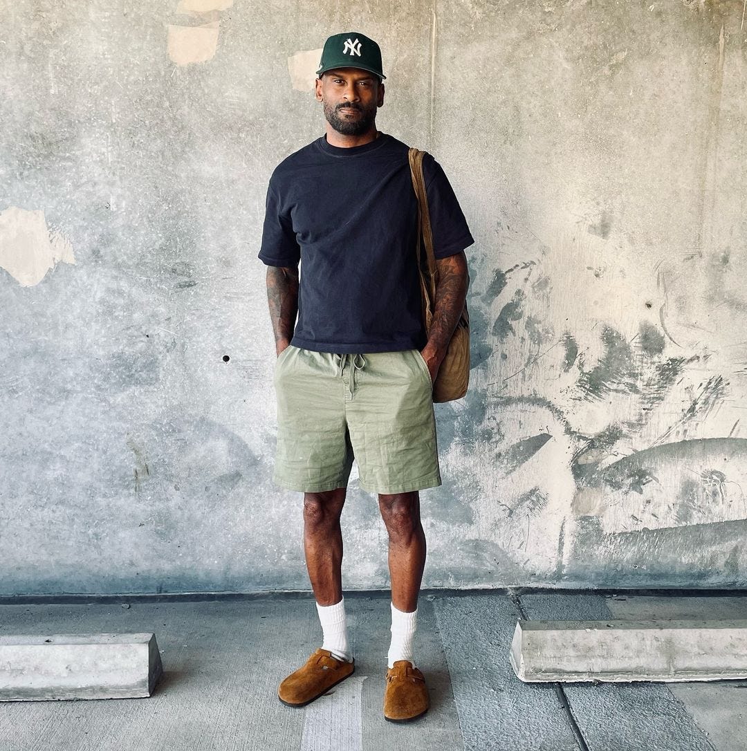 image of a man wearing a navy t-shirt, green drawstring shorts, tall white socks and brown Birkenstock clogs