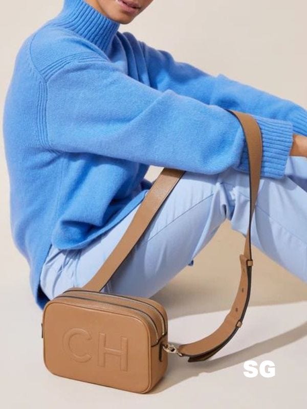 woman wearing a blue sweater, blue pants, and holding a purse with the letters "CH" monogrammed. onthe side