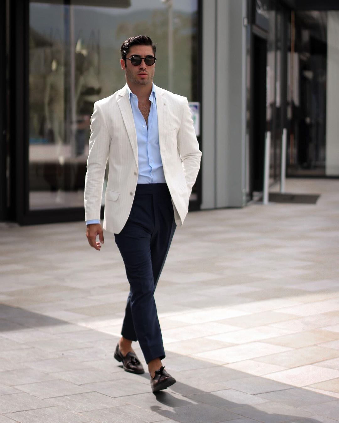 stylish man wearing a cream blazer with a light blue dress shirt, navy pants, and brown loafers