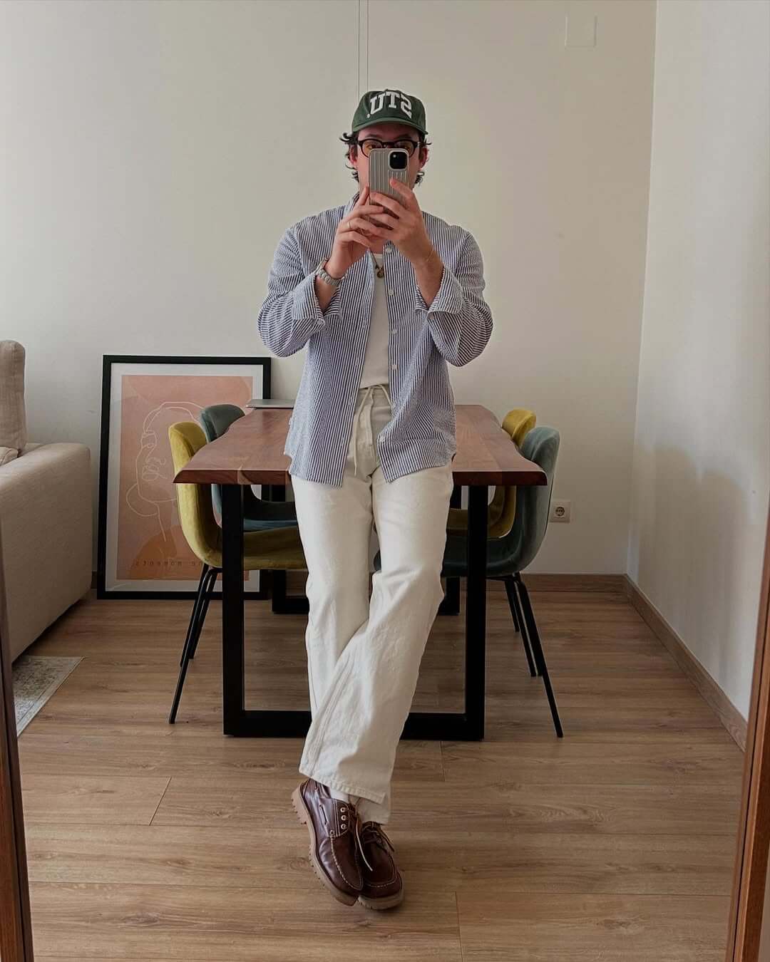 stylish man taking a selfie wearing a blue and white striped button down shirt over a white tee with white jeans and brown boat shoes
