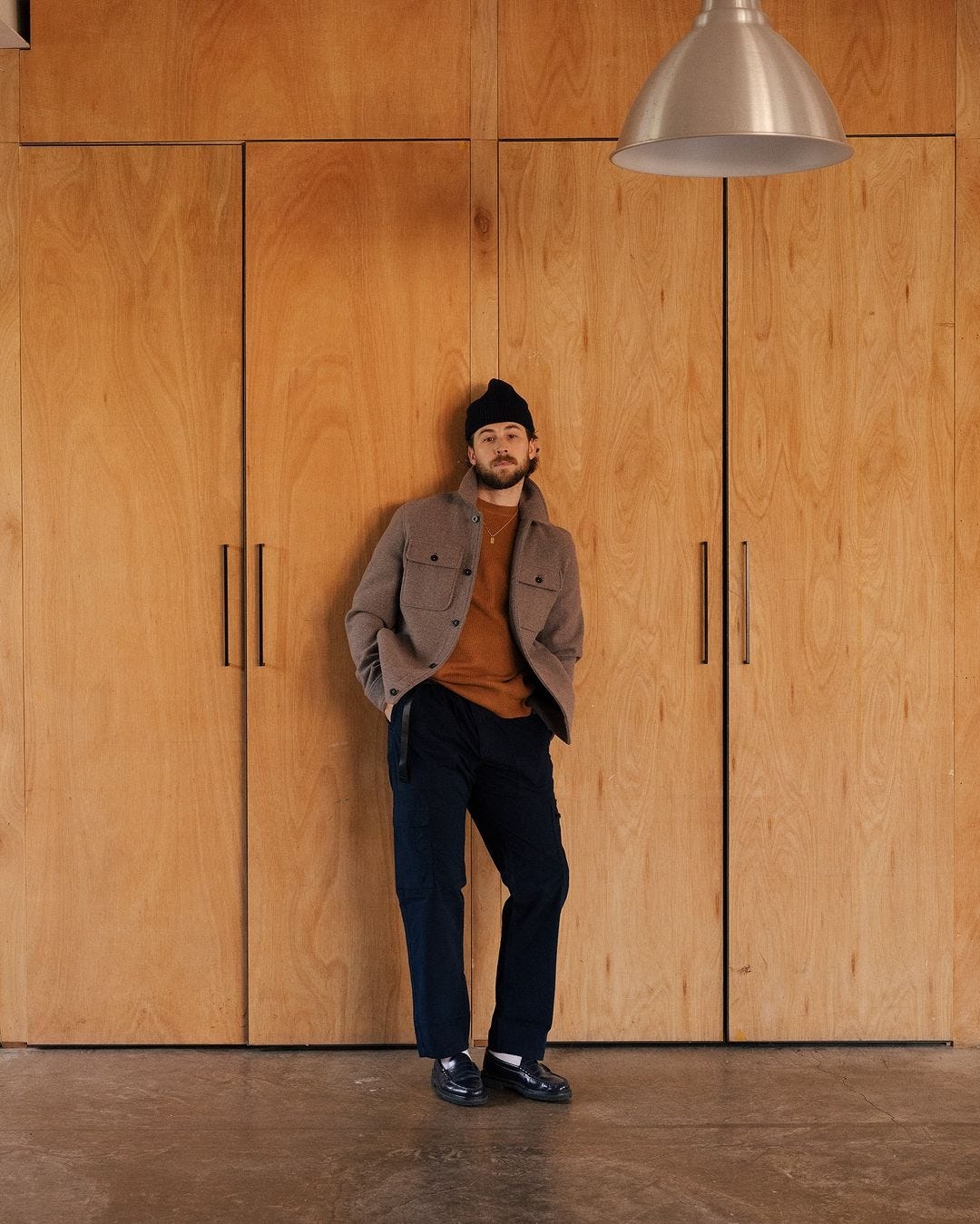 stylish man wearing a brown shirt jacket over a rust brown sweater with black pants and black loafers