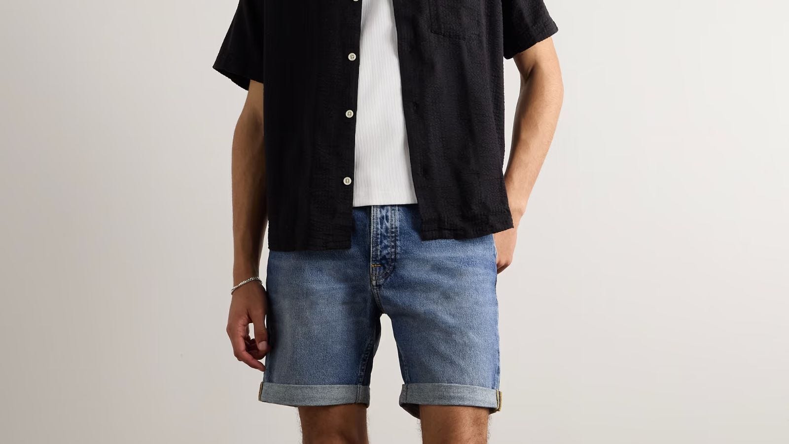 close-up of a man wearing a dark-colored short-sleeve shirt over a white t-shirt with jean shorts