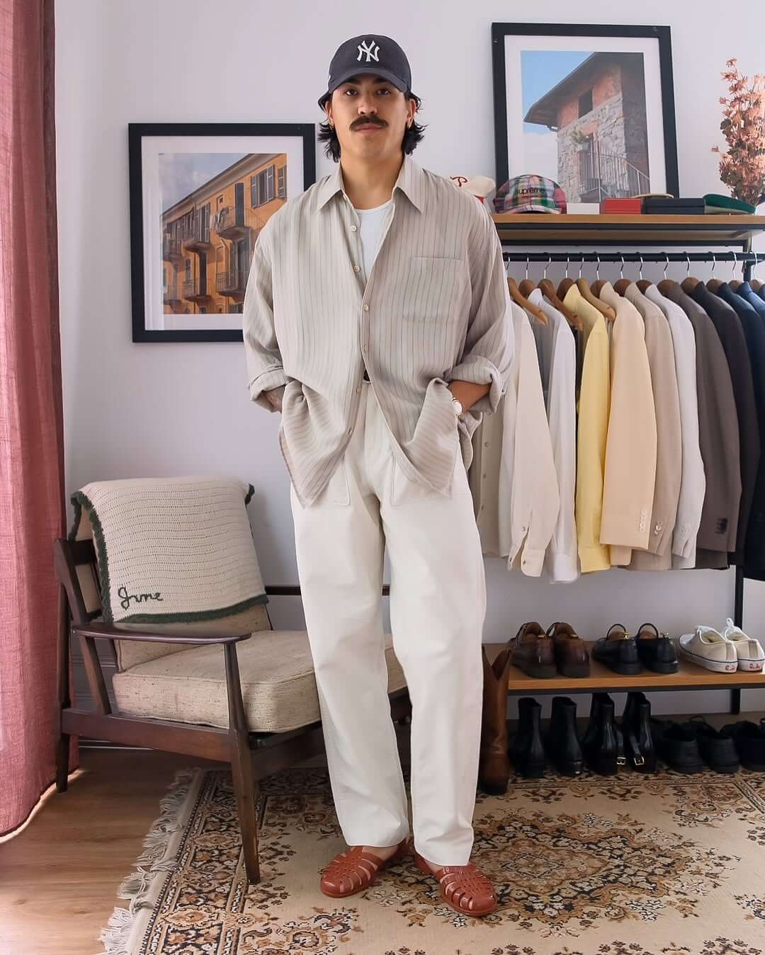 stylish man wearing a striped button-down shirt with baggy white jeans and a new york yankees baseball cap