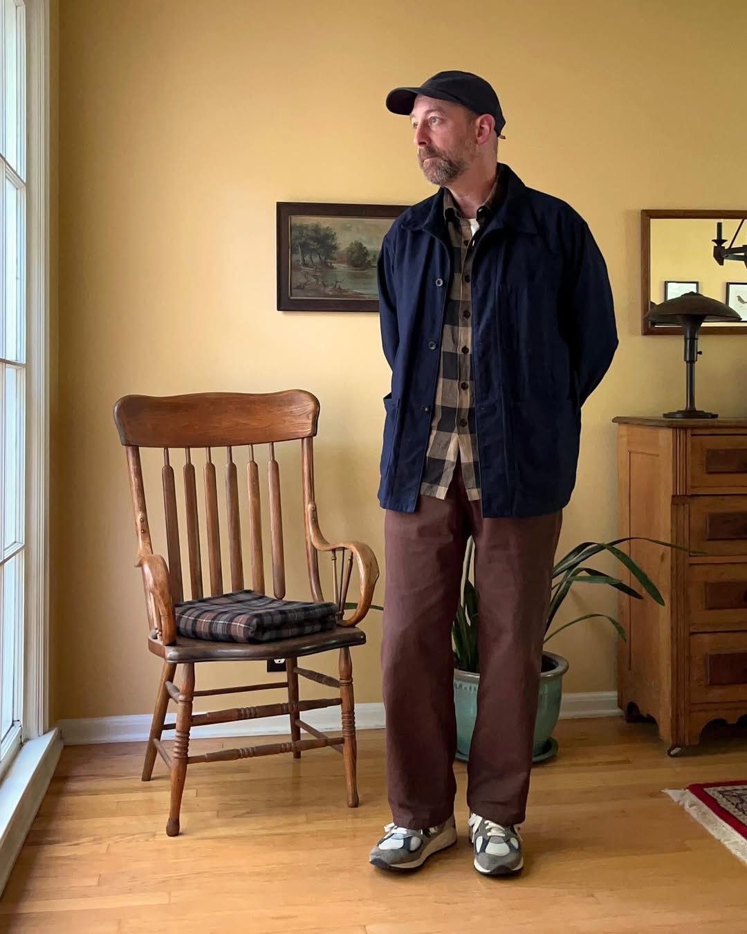 casually dressed man wearing a navy chore coat, plaid shirt, brown pants, and New Balance sneakers