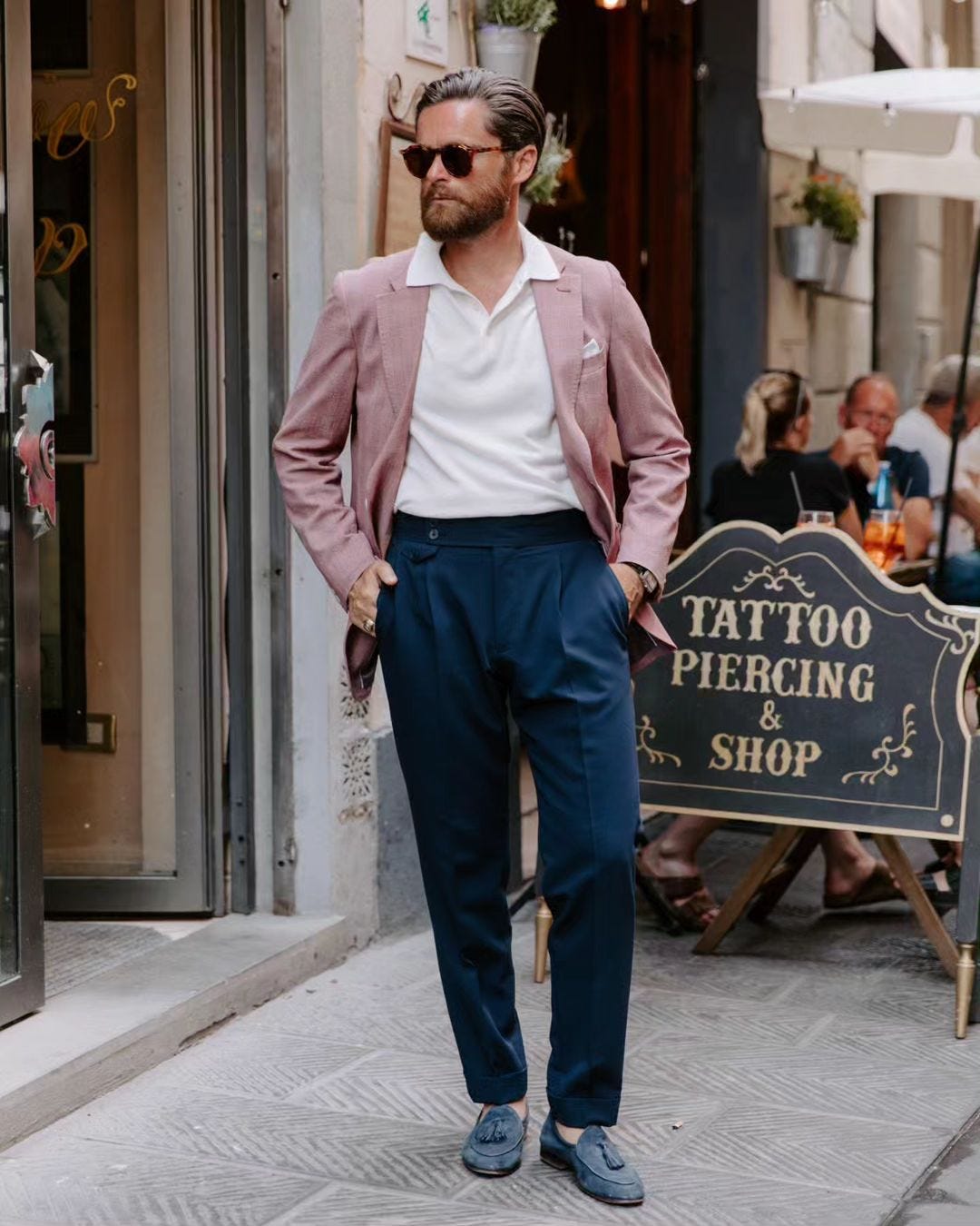 stylish man wearing an unstructured rose blazer, white knit polo and navy pleated pants