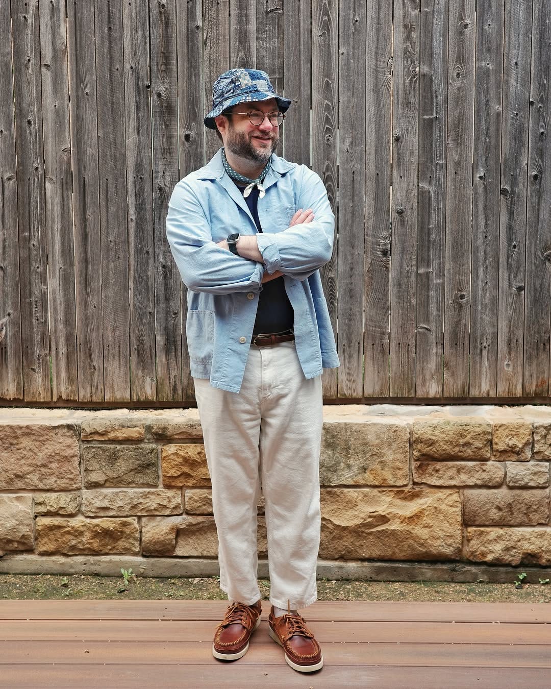 stylish man wearing a light blue chore coat with chinos, a bandana around his neck and brown leather sebago boat shoes