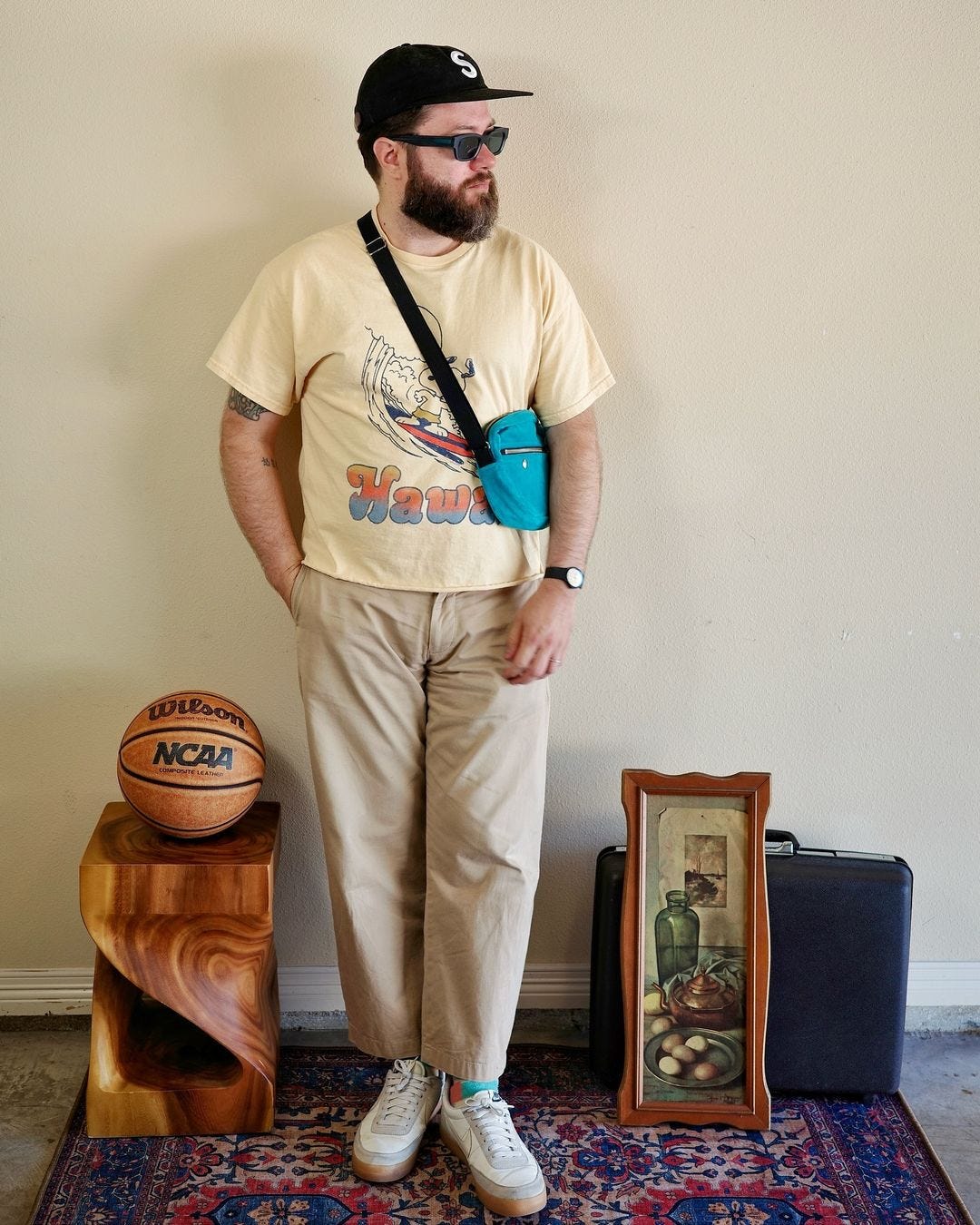 man wearing an off-white t-shirt, blue cross body bag, tan pants, and white sneakers