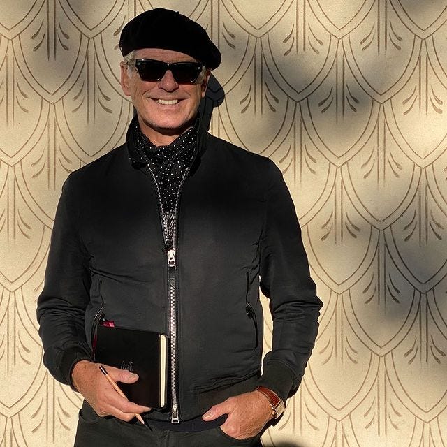 the actor Pierce Brosnan wearing a beret, sunglasses, and zipped jacket