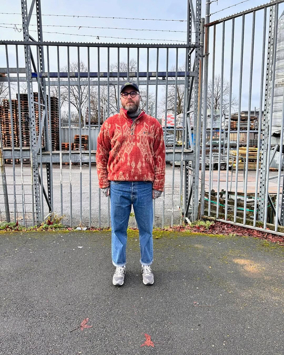 stylish man wearing a patterned red quarter zip fleece, blue jeans, and grey New Balance sneakers
