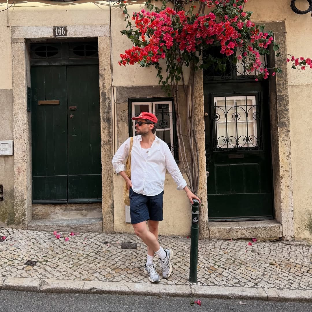 stylish man wearing a red cap, white shirt, navy shorts, and asics sneakers
