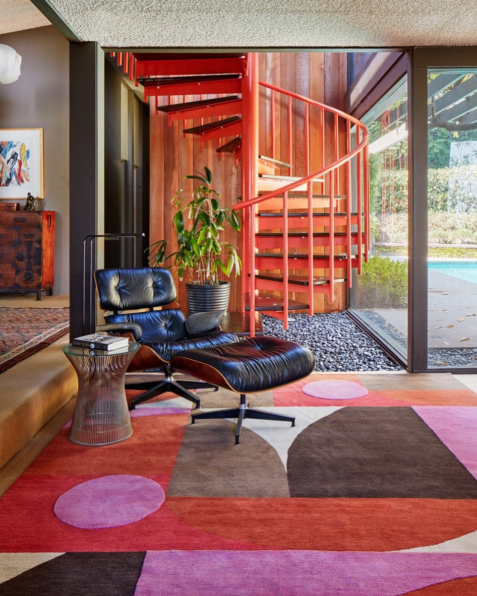 colorful living room with a black eames chair in front of a spiral staircase