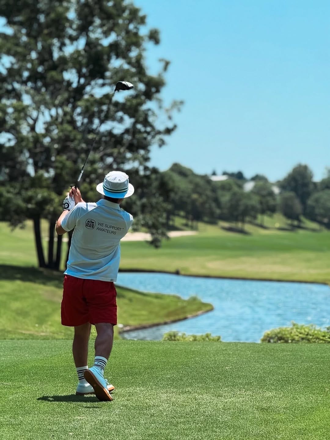 stylish man golfing, wearing a white polo shirt with red shorts