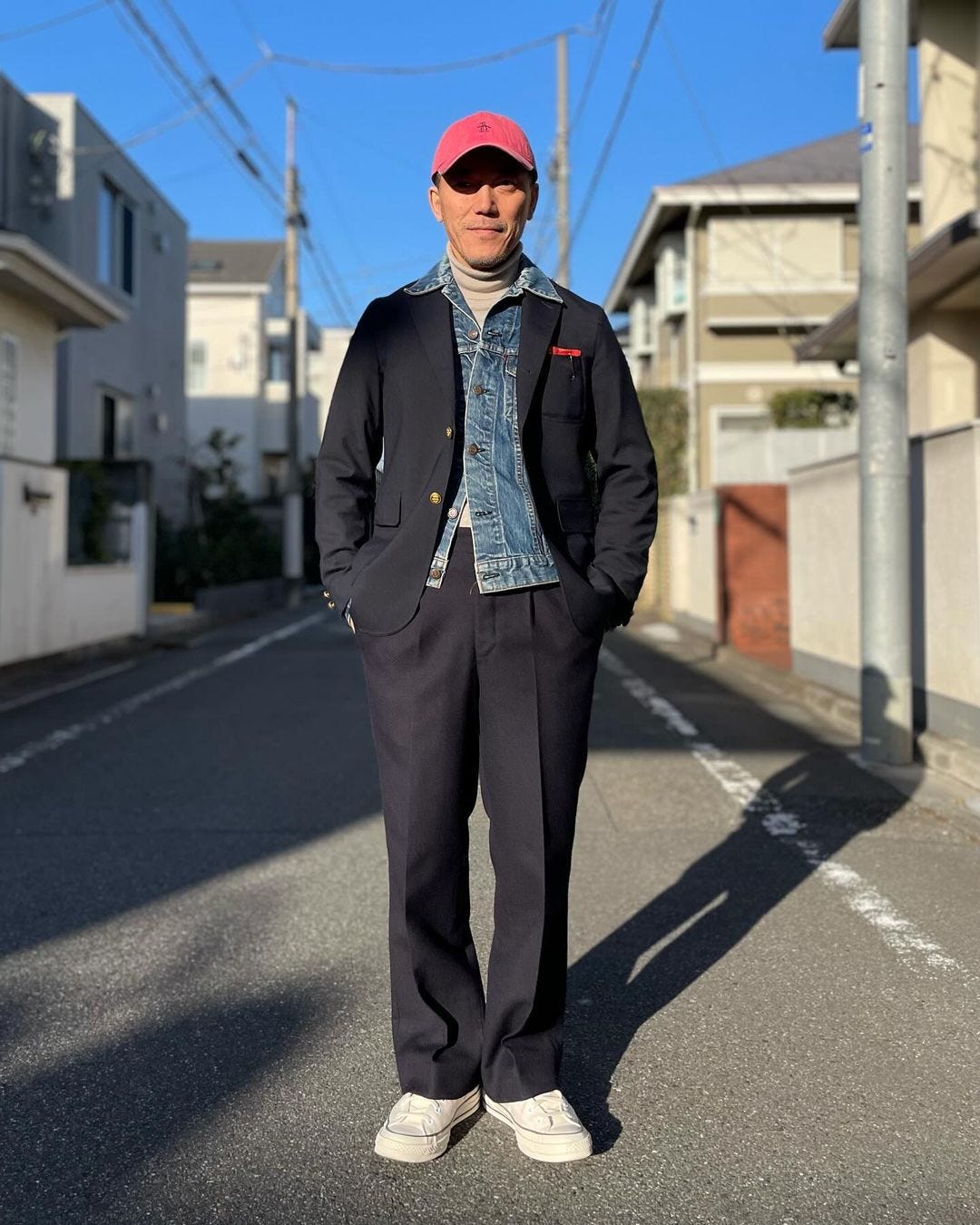 stylish man standing on a street wearing a navy blazer over a denim jacket over a turtleneck