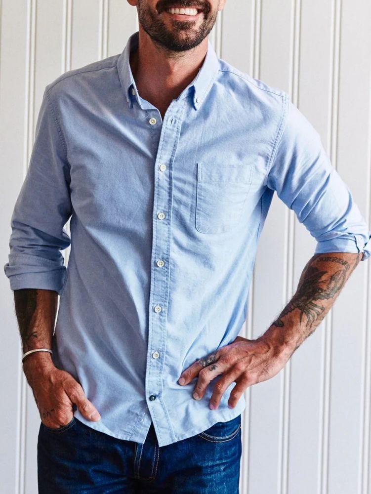 close-up of a man wearing a blue oxford shirt with the sleeves rolled up to reveal tattoos on his arms