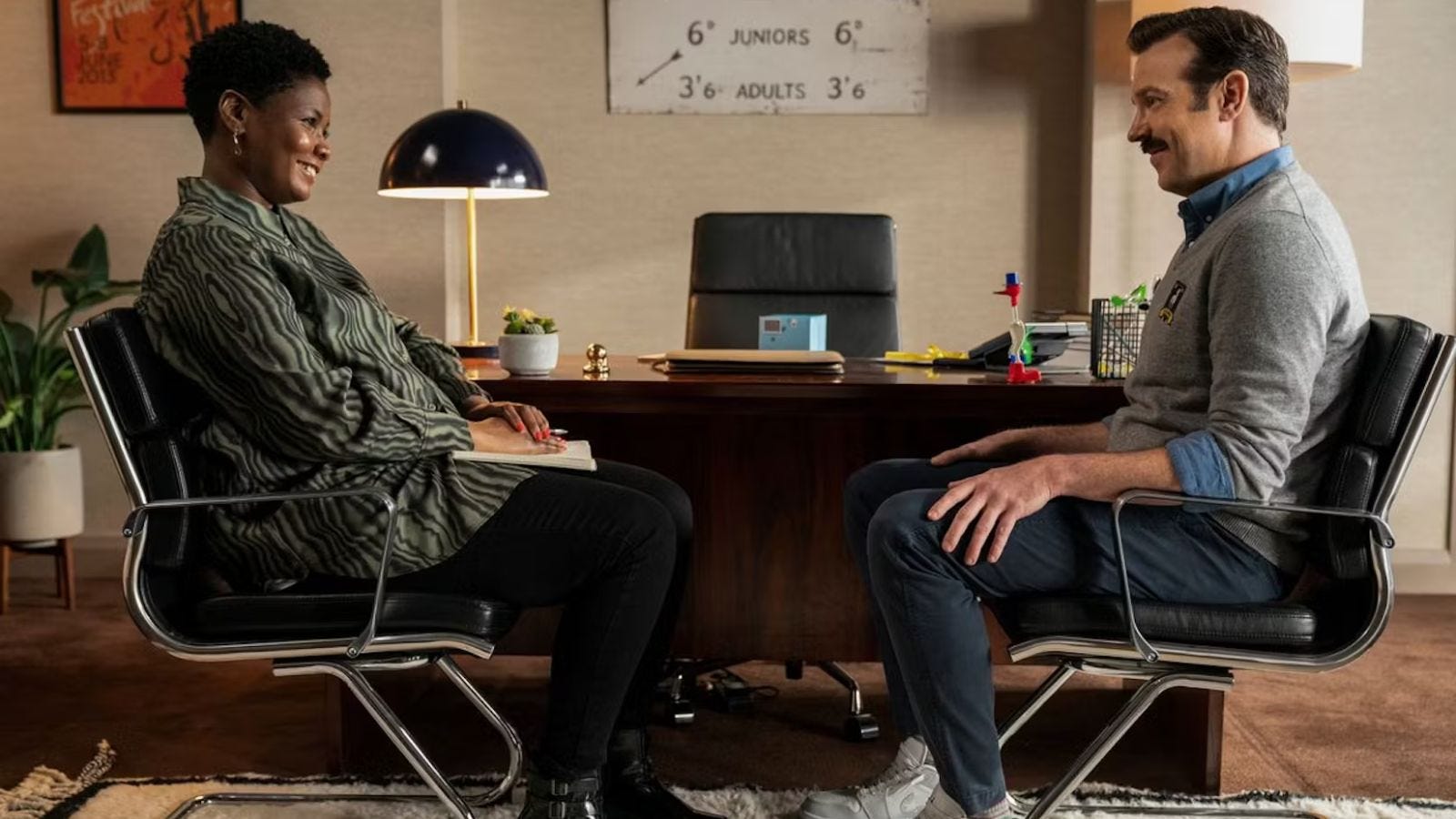 a still from the show Ted Lasso, where Ted is sitting across from his therapist. they are both smiling.