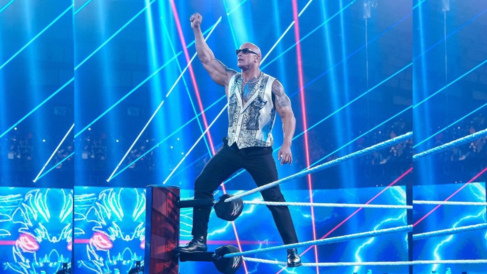 the rock standing in a wrestling ring wearing black pants and a gold vest