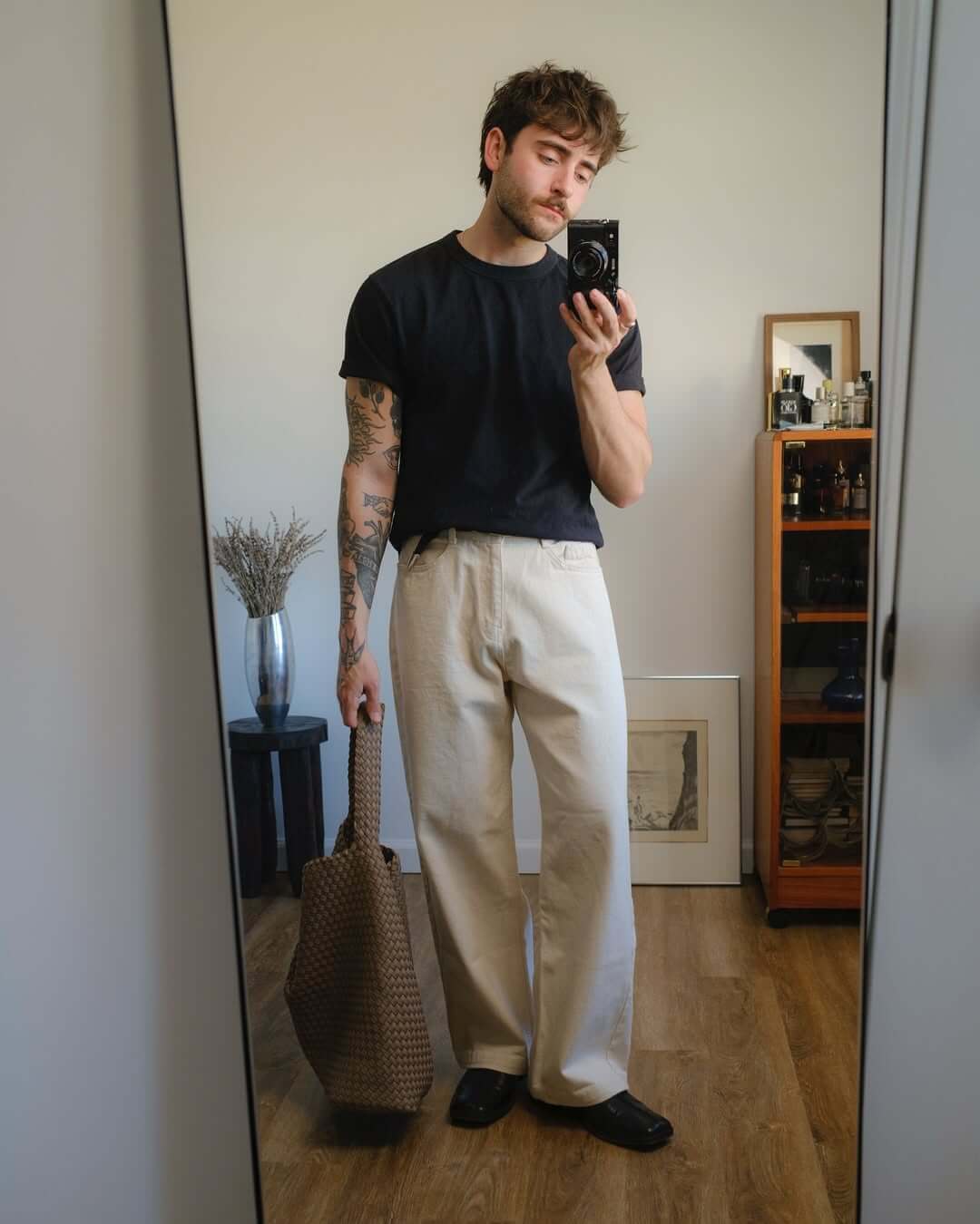 stylish man taking a selfie wearing a black t-shirt, white jeans, and dark shoes