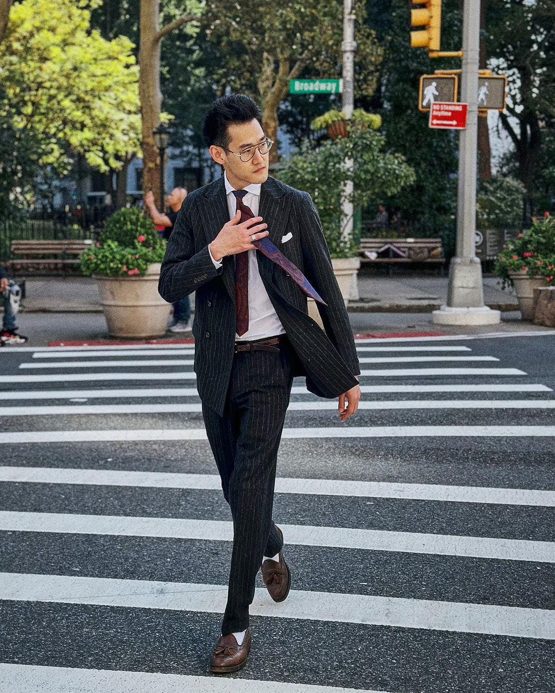 stylish man wearing a navy pinstripe suit with shirt and tie crossing a city street