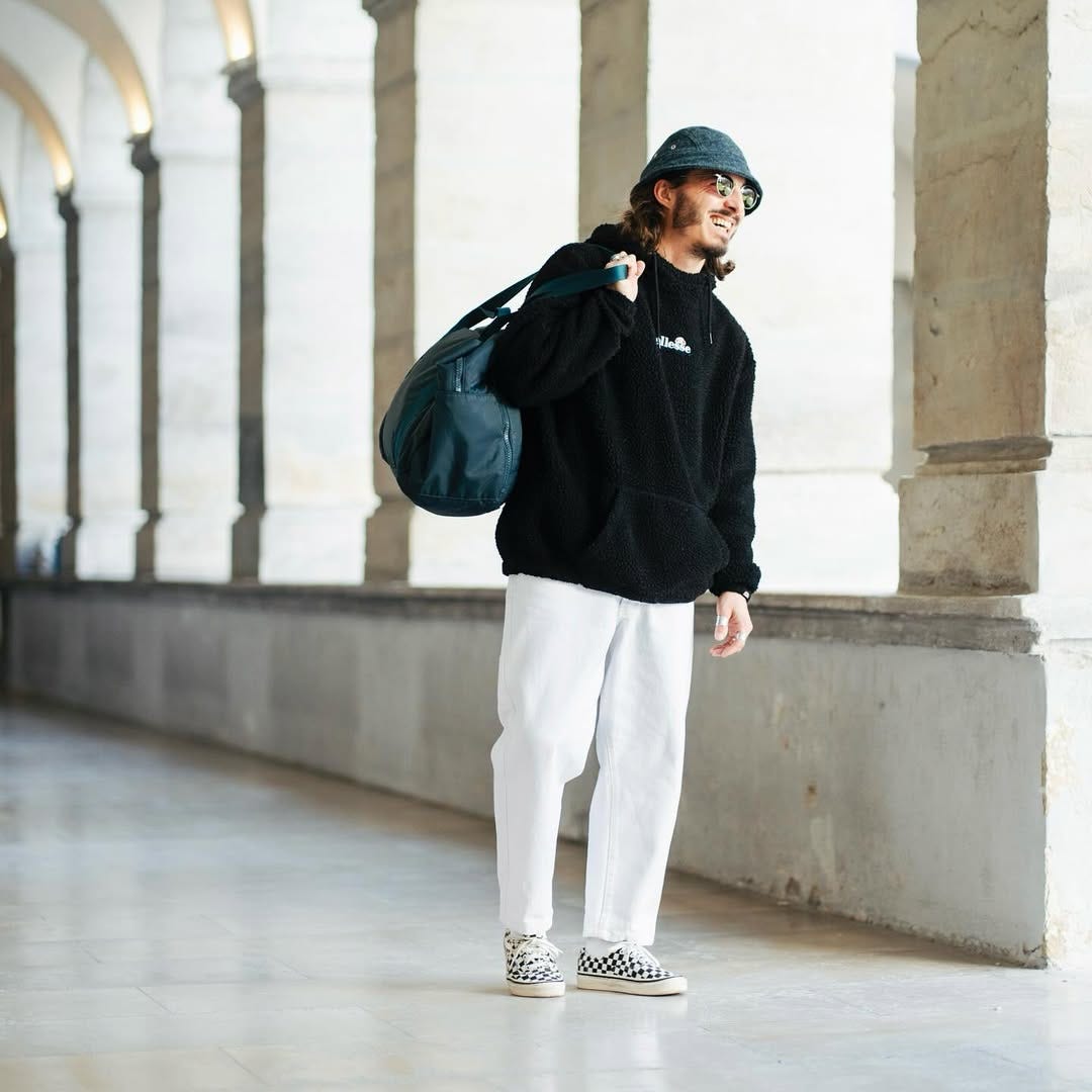 stylish man wearing a black hoodie with white jeans and black and white checkerboard lace-up vans sneakers