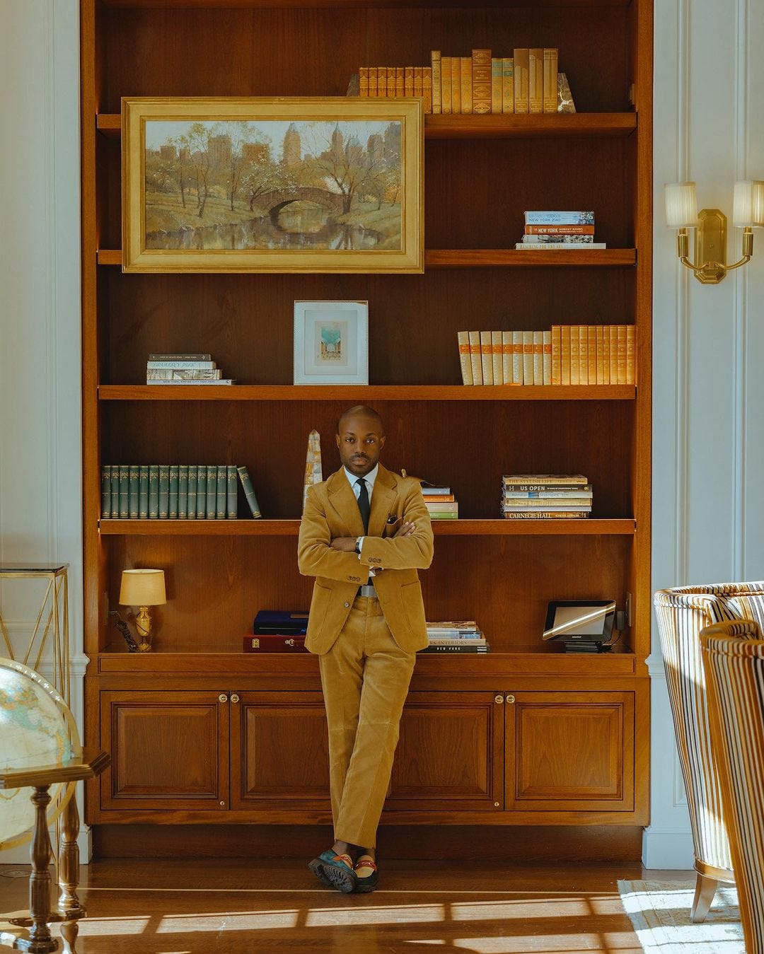 stylish man wearing a corduroy suit with shirt and tie, standing in front of a large bookshelf