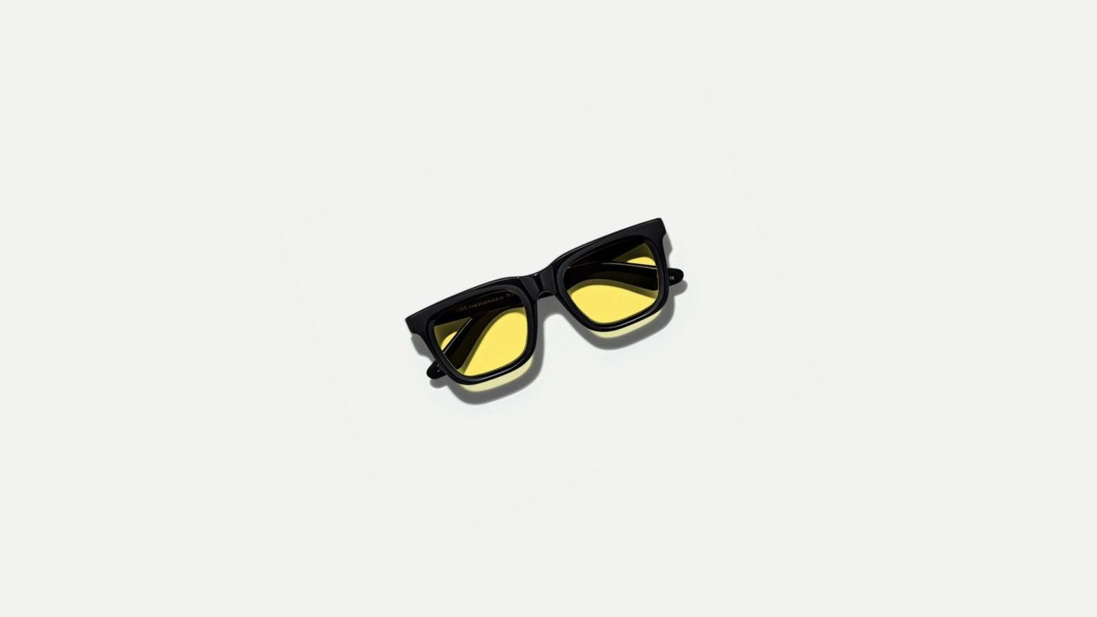 pair of black frame sunglasses with yellow lenses, folded up against a grey background